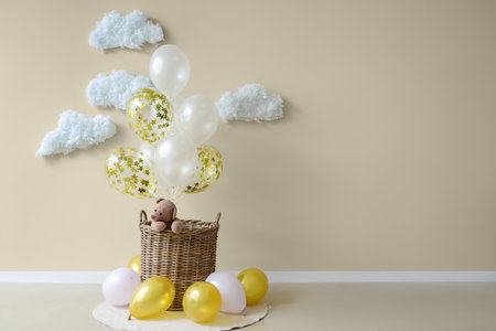 Basket with toy bear, balloons and cotton clouds near light wallの写真素材