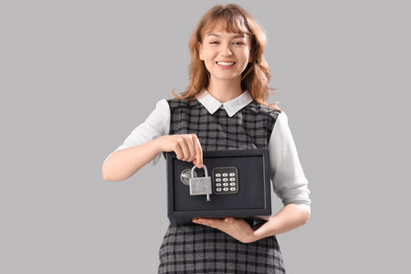 Beautiful young happy woman with safe box and lock on gray backgroundの写真素材
