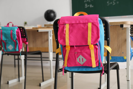 Schoolbag hanging on chair in classroom, closeup