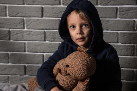 Homeless little boy with toy bear near gray brick wall, closeupの写真素材