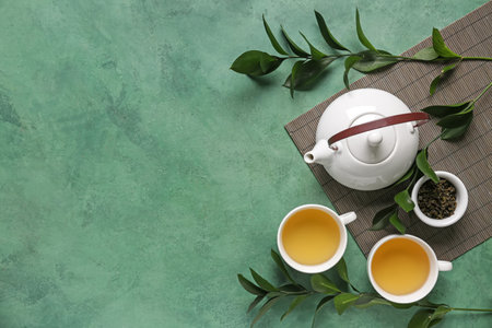 Teapot and cups of tea with leaves on green grunge backgroundの写真素材