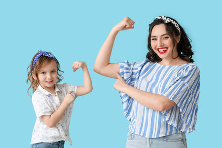 Beautiful pin-up woman and her daughter showing muscles on blue backgroundの写真素材