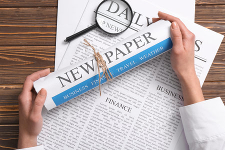 Female hands with magnifying glass and newspapers on wooden background