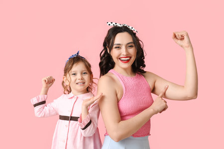 Beautiful pin-up woman and her daughter showing muscles on pink background