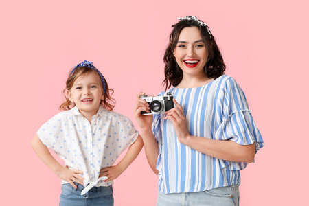 Beautiful pin-up woman with photo camera and her daughter on pink backgroundの写真素材
