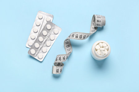 Bottle with weight loss pills, blister packs and measuring tape on blue backgroundの写真素材