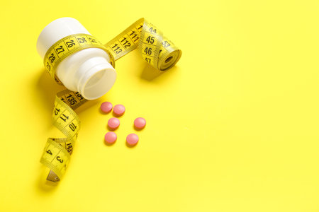 Bottle with weight loss pills and measuring tape on yellow backgroundの写真素材