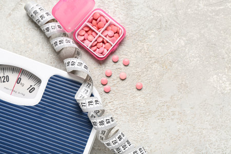 Container with weight loss pills, scales and measuring tape on gray grunge backgroundの写真素材