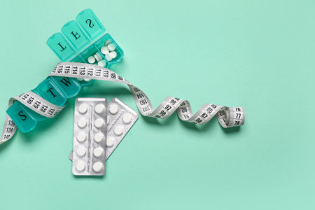 Container, blister packs with weight loss pills and measuring tape on turquoise backgroundの写真素材