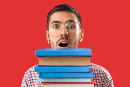 Young man with stack of books on red backgroundの写真素材
