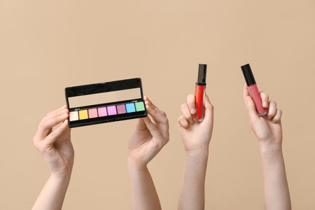 Female hands with eyeshadows palette and lipsticks on beige backgroundの写真素材