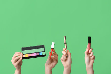Female hands with eyeshadows palette, mascara and lipsticks on green backgroundの写真素材