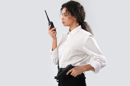 African-American female police officer with radio transmitter and gun on white background