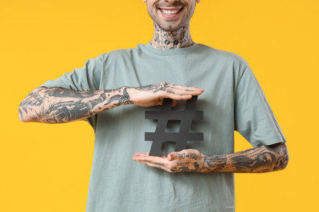 Cool tattooed young man with hashtag symbol on yellow backgroundの写真素材