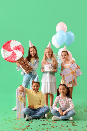 Cute little children in party hats with Birthday gifts, cake and pinata on green backgroundの写真素材