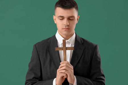 Young man with wooden cross praying on green backgroundの写真素材