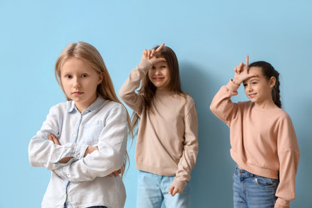 Bullied little girl and her classmates showing loser gesture on blue backgroundの写真素材