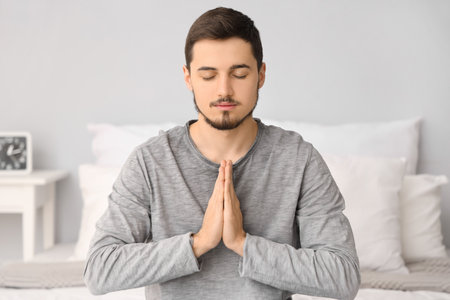 Young man praying in bedroomの写真素材