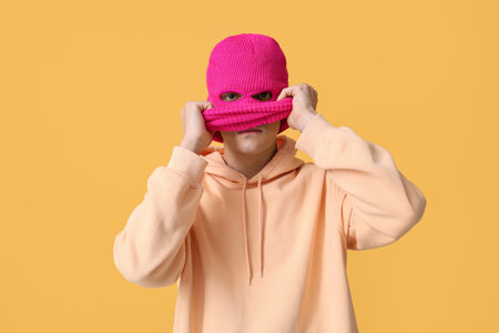 Handsome young man in balaclava on yellow background