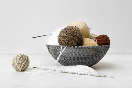 Basket with yarn balls and knitting needles on white background