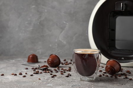 Glass of delicious espresso, capsule coffee maker, pods and beans on gray grunge tableの写真素材