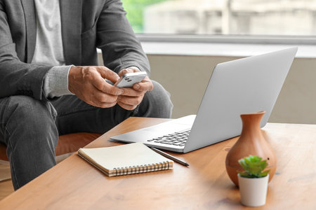 Mature businessman with mobile phone messaging in office, closeupの写真素材