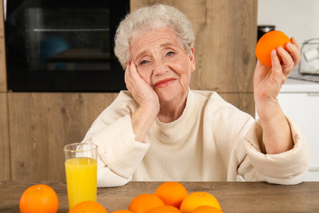 Senior woman with orange and glass of juice in kitchenの写真素材