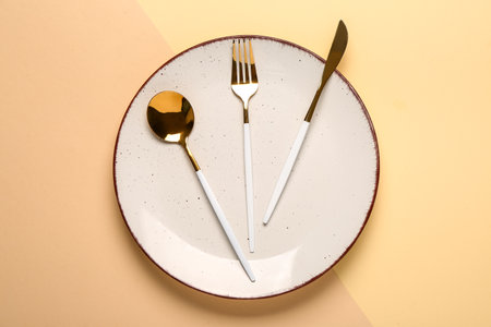 Clean plate with set of golden cutlery on beige background, closeupの写真素材