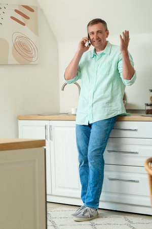 Mature man talking by mobile phone in kitchenの写真素材