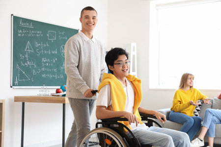 Teenage boy with his classmate in wheelchair at schoolの写真素材