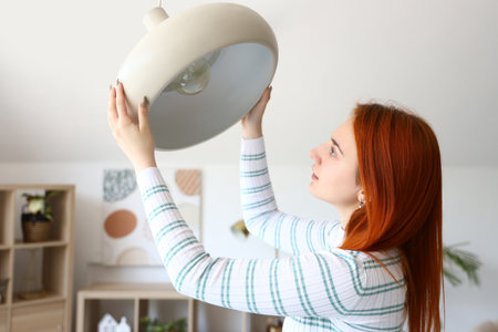 Pretty young woman changing light bulb in lamp at homeの写真素材