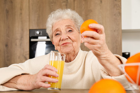 Senior woman with glass of juice and orange in kitchenの写真素材