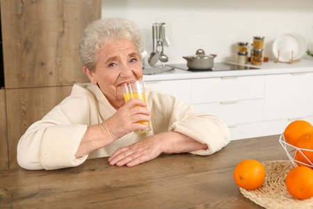 Senior woman drinking orange juice in kitchenの写真素材