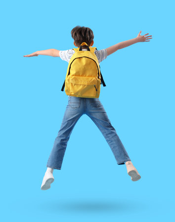 Jumping little boy with schoolbag on blue background, back viewの写真素材