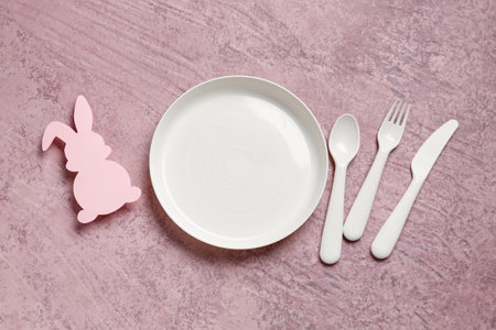 Plate with eating utensils for baby and paper rabbit on grunge pink backgroundの写真素材