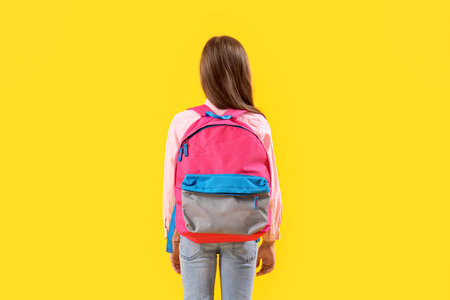 Little girl with schoolbag on yellow background, back viewの写真素材