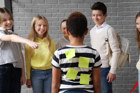 Bullied little boy with sticky papers on his back at school