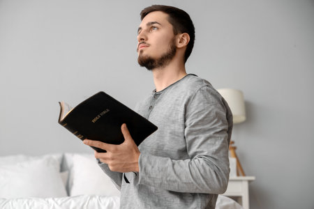 Young man reading Bible in bedroomの写真素材