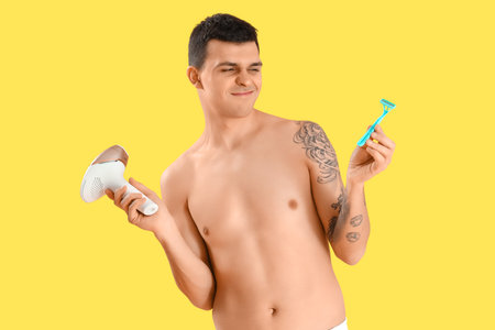 Young man choosing between photoepilation and shaving on yellow backgroundの写真素材