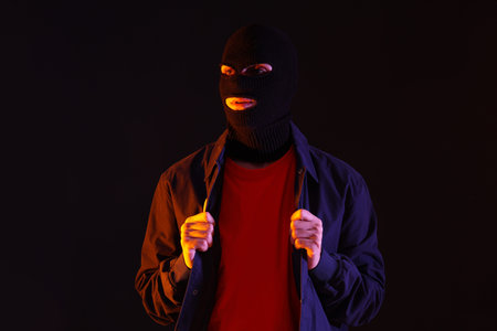 Handsome young man in balaclava on black background