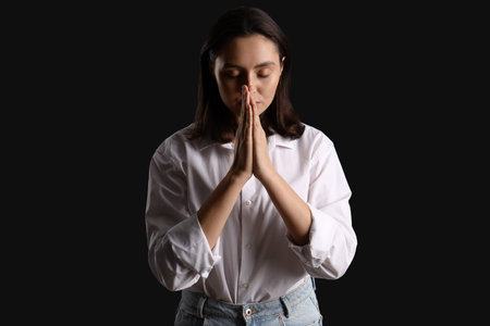 Young woman praying on black background
