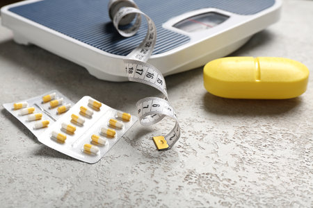 Container with weight loss pills, scales and measuring tape on gray grunge backgroundの写真素材