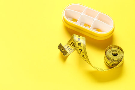 Container with weight loss pills and measuring tape on yellow backgroundの写真素材