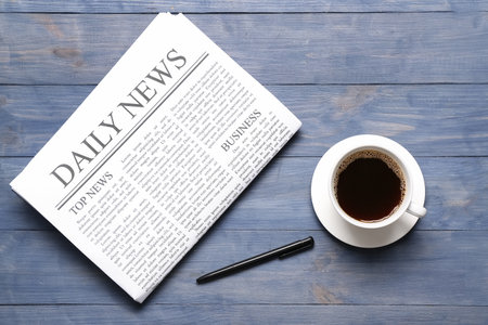 Newspaper with cup of coffee and pen on blue wooden backgroundの写真素材