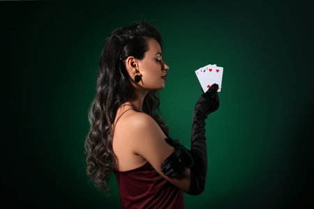 Beautiful young African-American woman with playing cards on dark green background