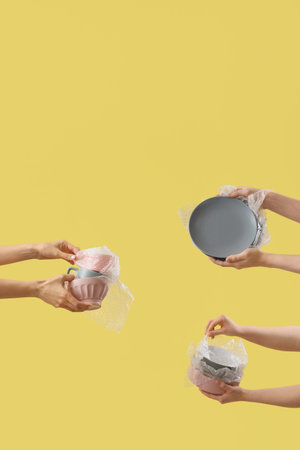Women with wrapped dishes on yellow background. Moving concept