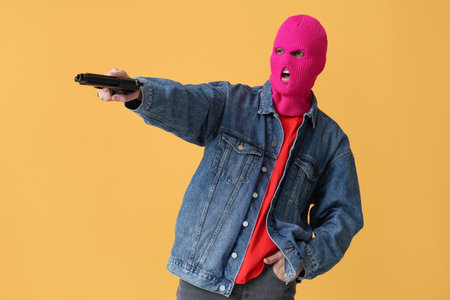 Handsome young man in balaclava with gun on yellow backgroundの写真素材