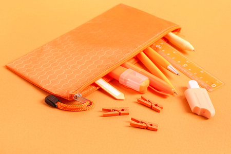 Pencil case with different school stationery on orange background