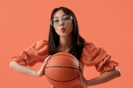 Young Asian woman with basketball on orange backgroundの写真素材