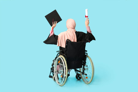 Beautiful female Muslim graduate student in wheelchair with graduation cap and diploma on blue...